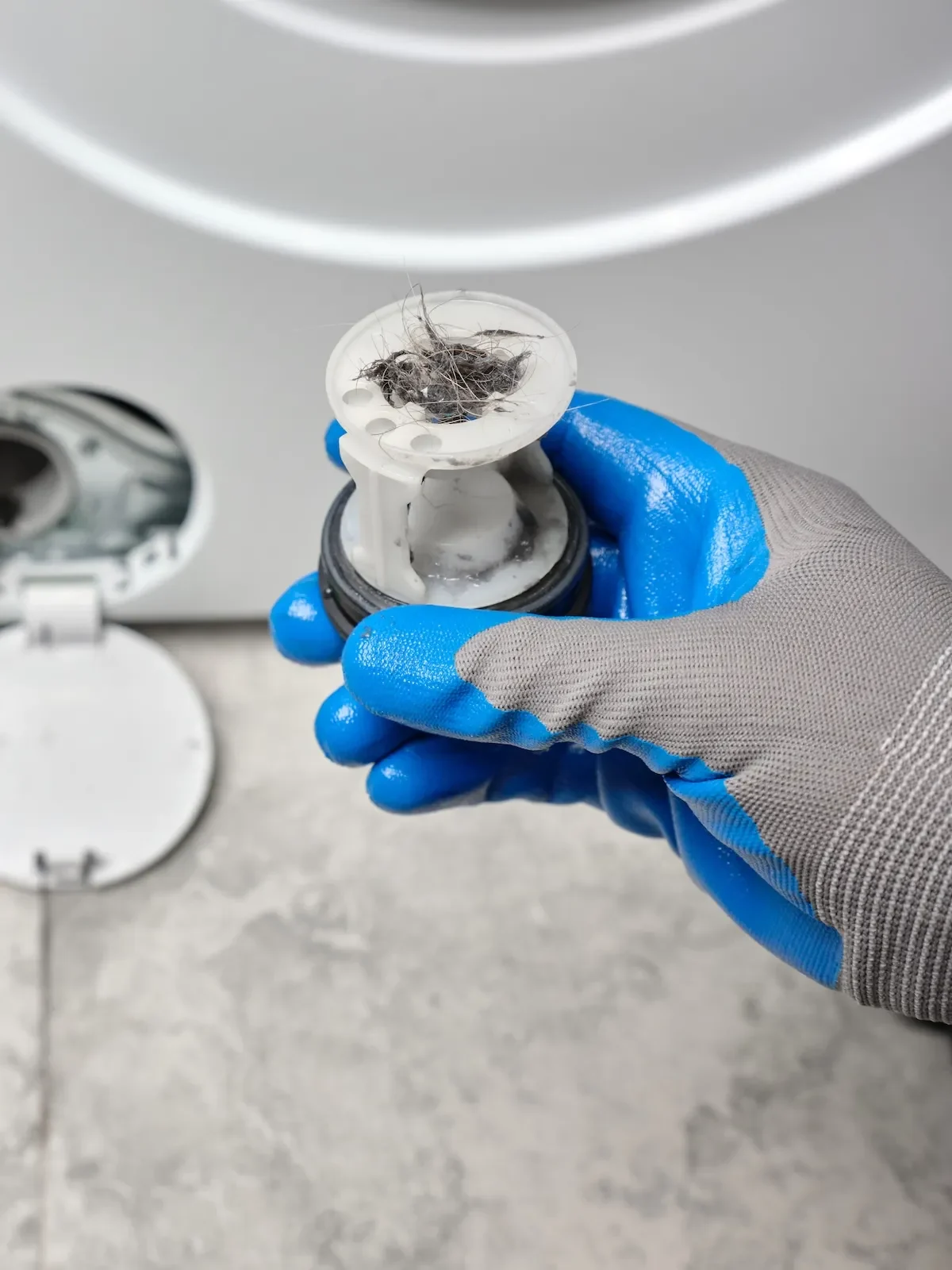 A hand removing the filter from a washing machine.