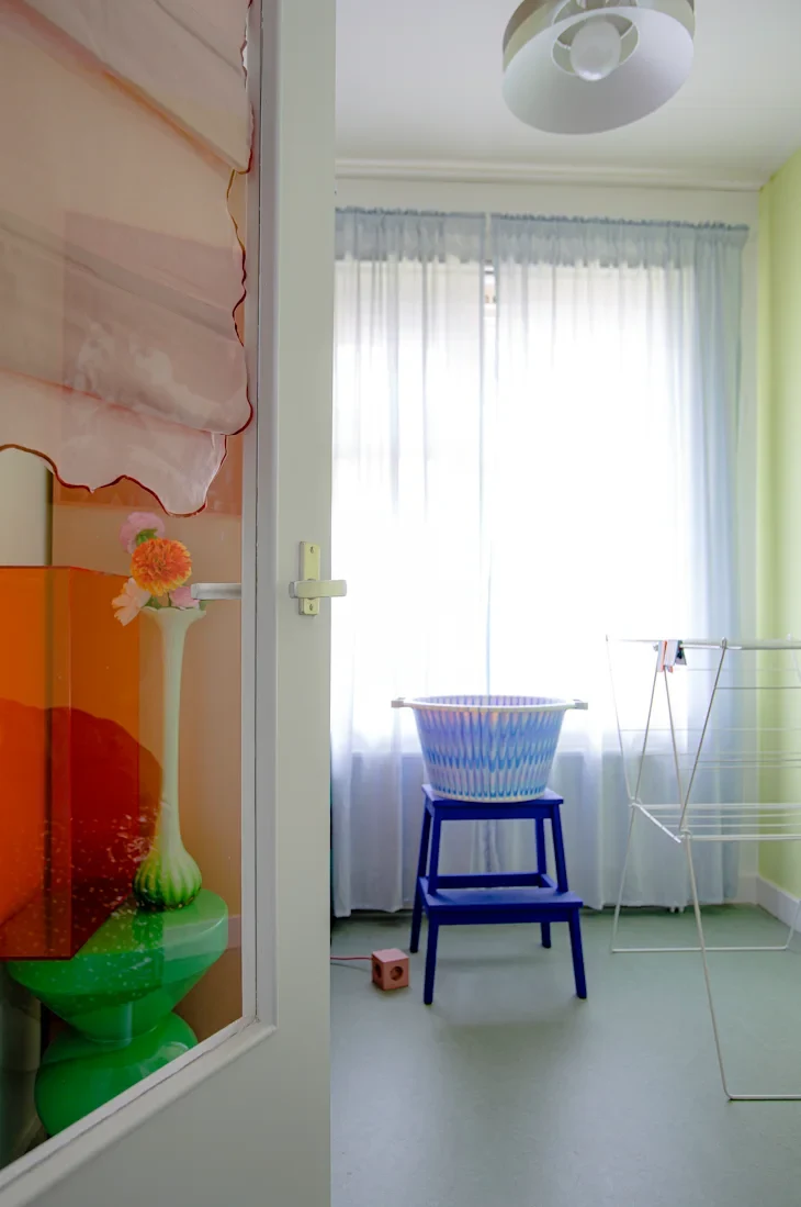 Bright room with sheer curtains, a blue chair, a patterned laundry basket, and a drying rack.