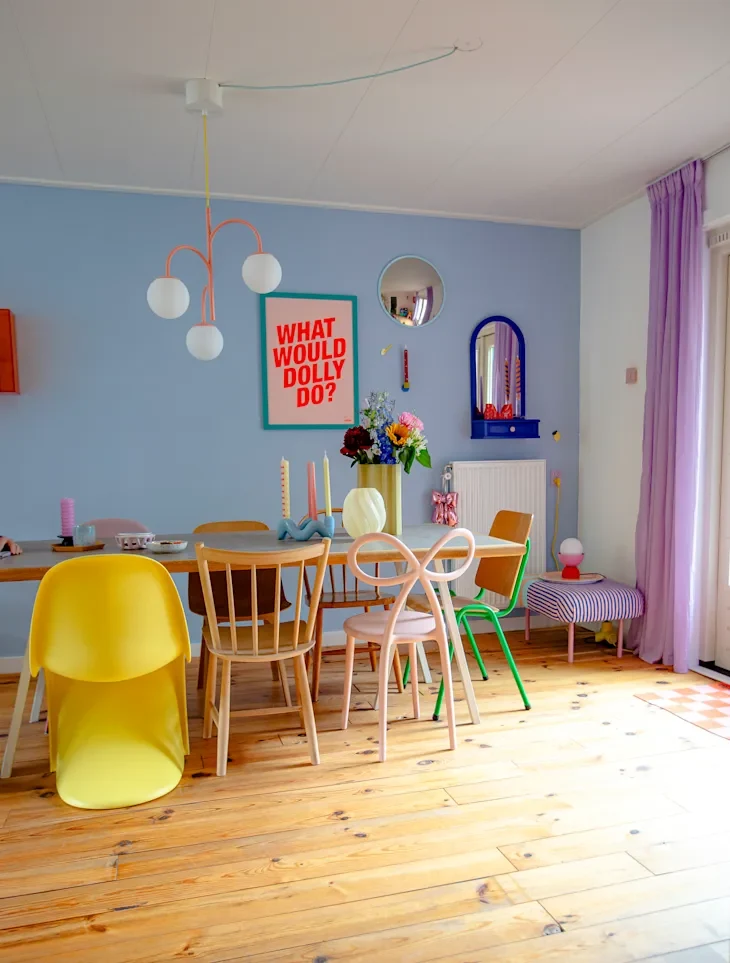 Colorful dining area featuring a wooden table, various chairs, a vibrant poster, and floral decor.
