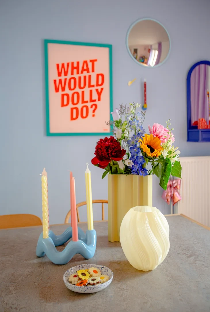 Colorful floral arrangement in a yellow vase, blue candle holder with three candles, and decorative plate with cookies.