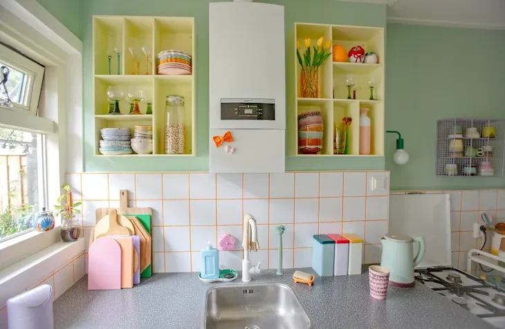 Colorful kitchen with open shelves displaying glassware, plates, and decorative items, alongside a sink and cutting boards.