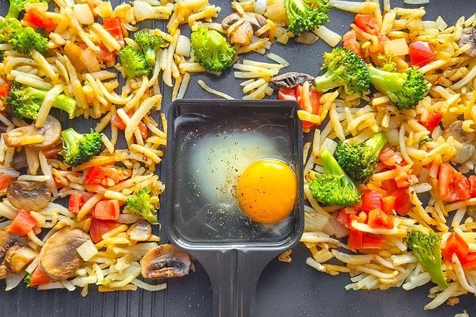egg in Raclette Paddle in front of cooked vegetables on a grill